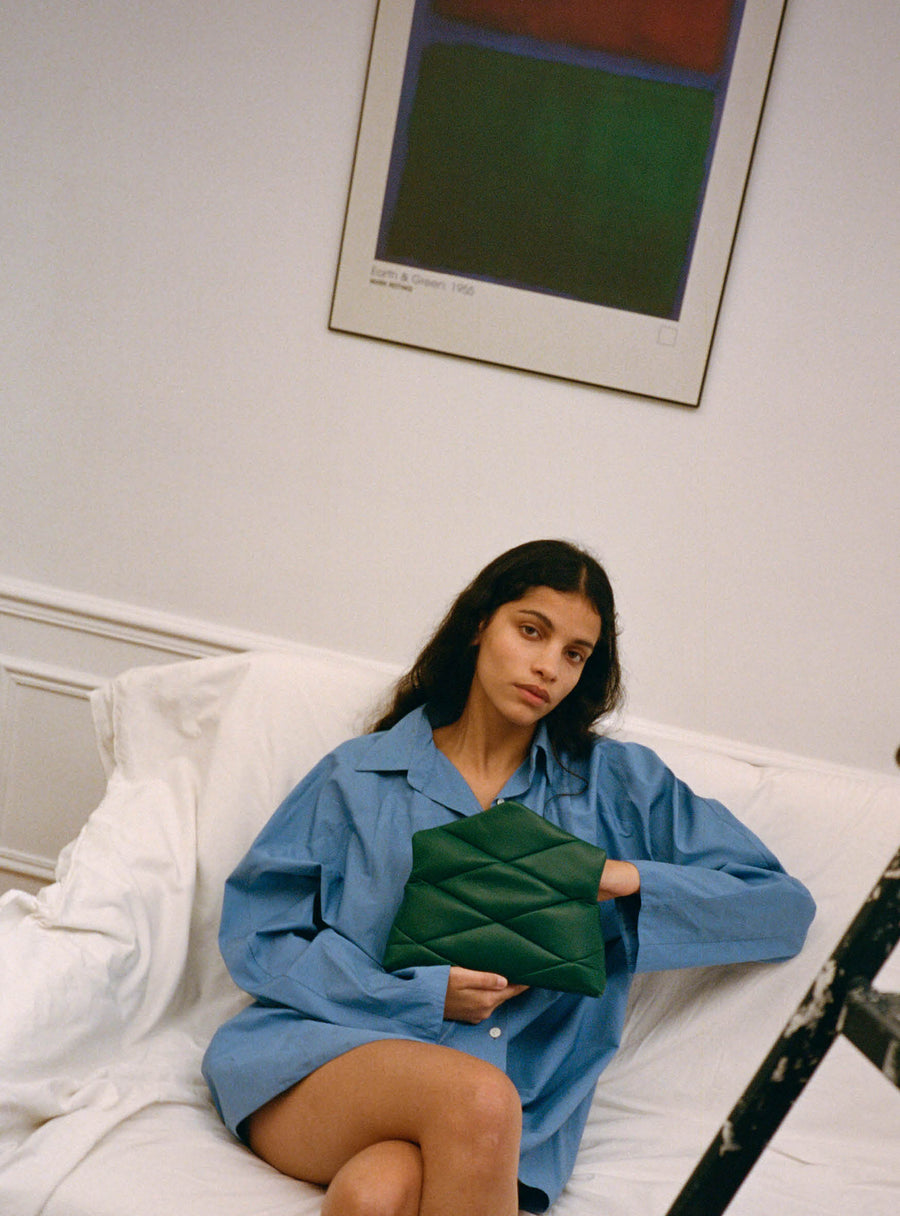 Woman sitting on a sofa with a dark green leather handbag in her hands